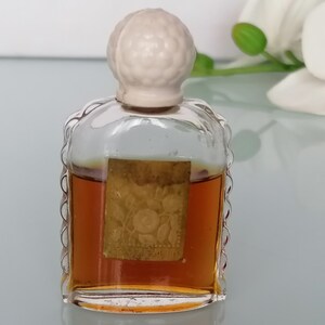 May include: A small, clear glass bottle with a white plastic stopper. The bottle contains a brown liquid and has a gold label with a floral design.