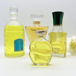 Op de afbeelding: Vier flessen parfum, allemaal in verschillende vormen en maten. De flessen zijn gevuld met een gele vloeistof en hebben verschillende etiketten. De flessen staan op een wit oppervlak.