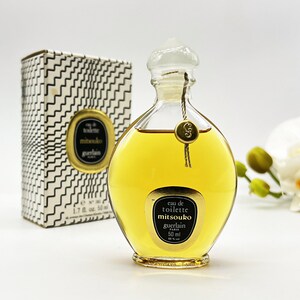 May include: A vintage bottle of Mitsouko Eau de Toilette by Guerlain. The bottle is clear glass with a gold cap and a gold label. The label reads "eau de toilette mitsouko guerlain paris 50 ml".