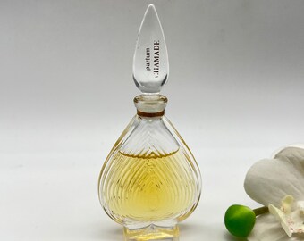 May include: A clear glass bottle of perfume with a heart-shaped base and a pointed stopper. The bottle is filled with a yellow liquid and the stopper has the text "parfum HAMAMADE" printed on it.