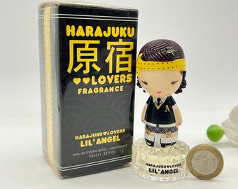 May include: A small bottle of Harajuku Lovers Lil' Angel perfume with a black and yellow box. The bottle is shaped like a doll with a black and white plaid skirt, a yellow headband, and a black shirt with a gold letter A. The bottle is sitting on a coin.