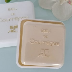 Puede incluir: Dos cajas cuadradas blancas con letras doradas. La caja superior dice "eau de Courr&egrave;ges" y la caja inferior dice "eau de Courr&egrave;ges". Ambas cajas tienen un logotipo "C" dorado.