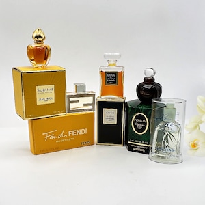 以下が含まれることがあります： 様々な色とデザインのミニチュア香水瓶のコレクション。瓶は白い表面に並べられています。瓶には、ジャン・パトゥのサブライム、ファン・ディ・フェンディ、ココ・シャネル、ココ・シャネル、ポイズン・クリスチャン・ディオール、フルール・ド・ロカイユが含まれています。