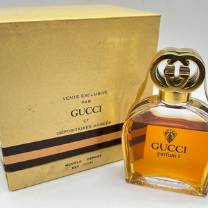 May include: A gold and brown box with the text "Vente Exclusive Par Gucci Et D&eacute;positaire Agr&eacute;es" and a clear glass bottle of Gucci perfume with a gold cap and the text "Gucci Parfum 1".