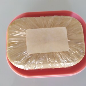May include: A bar of soap wrapped in plastic and a label, sitting in a pink soap dish.