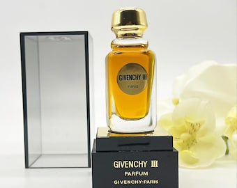 May include: A Givenchy III perfume bottle with a gold cap and a gold label. The bottle is filled with a golden liquid and sits on a black box with gold lettering. The box reads "Givenchy III Parfum Givenchy-Paris."