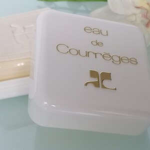 Puede incluir: Pastilla de jab&oacute;n blanca en un recipiente de pl&aacute;stico blanco con un logotipo dorado y el texto "eau de Courr&egrave;ges" en la tapa.