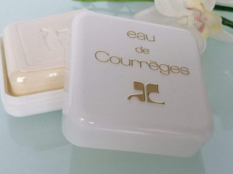 Puede incluir: Pastilla de jab&oacute;n blanca en un recipiente de pl&aacute;stico blanco con un logotipo dorado y el texto "eau de Courr&egrave;ges" en la tapa.