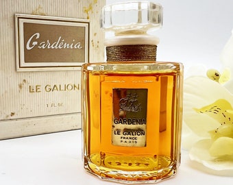 May include: A vintage bottle of Gardenia Le Galion perfume. The bottle is clear glass with a gold label and a gold cap. The bottle is filled with a yellow liquid. The label reads "Gardenia Le Galion France Paris".