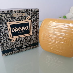 Może przedstawiać: Czarne i złote pudełko z nadrukiem "SOAP", "DRAKKAR", "FOR MEN" i "GUY LAROCHE PARIS". Obok pudełka znajduje się mydło.