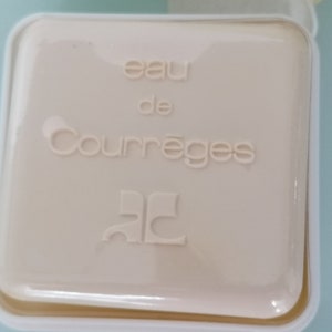 Puede incluir: Una caja cuadrada blanca con el texto "eau de Courr&egrave;ges" y el logotipo "CC" en una fuente estilizada.