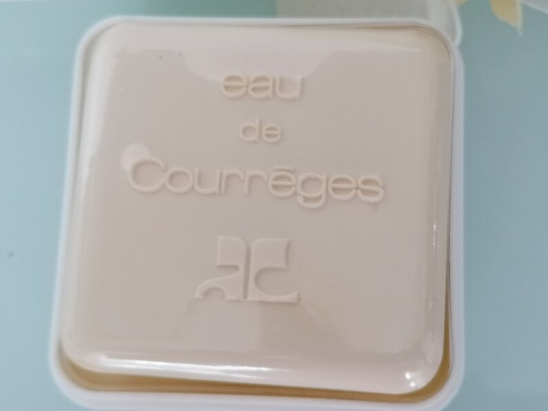 Puede incluir: Una caja cuadrada blanca con el texto "eau de Courr&egrave;ges" y el logotipo "CC" en una fuente estilizada.