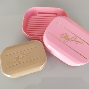 May include: A pink soap dish with gold lettering that reads "Olga Cassini II" and a matching beige bar of soap with the same lettering.