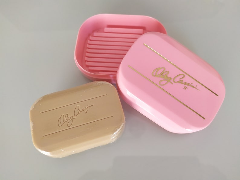 May include: A pink soap dish with gold lettering that reads "Olga Cassini II" and a matching beige bar of soap with the same lettering.