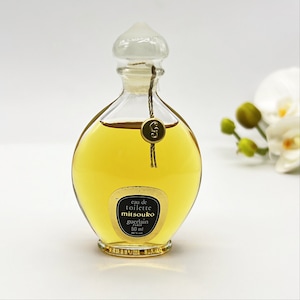 May include: A clear glass bottle of Mitsouko Eau de Toilette by Guerlain. The bottle has a gold cap and a gold label with black text. The label reads "eau de toilette mitsouko guerlain 50 ml".