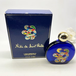 Puede incluir: Una botella azul de aceite de ba&ntilde;o perfumado L'Huile Essentielle de Niki de Saint Phalle. La botella tiene una tapa dorada y un dise&ntilde;o de serpiente colorido. La botella es de 3,4 fl oz o 100 ml.