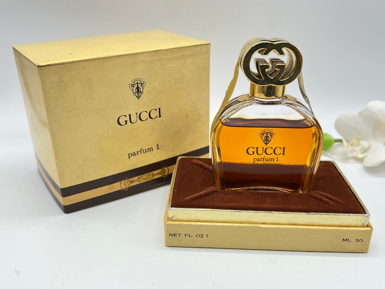 May include: A vintage Gucci perfume bottle with a gold cap and a brown box. The bottle is filled with a golden liquid and the box has the Gucci logo and the text "parfum 1" printed on it. The bottle is 1 fluid ounce and the box is 30 ml.