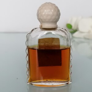 May include: A small, clear glass bottle with a white plastic stopper. The bottle is filled with a brown liquid and has a label on the front.
