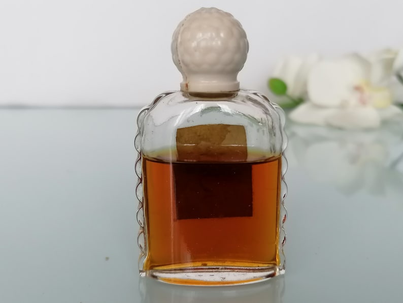 May include: A small, clear glass bottle with a white plastic stopper. The bottle is filled with a brown liquid and has a label on the front.
