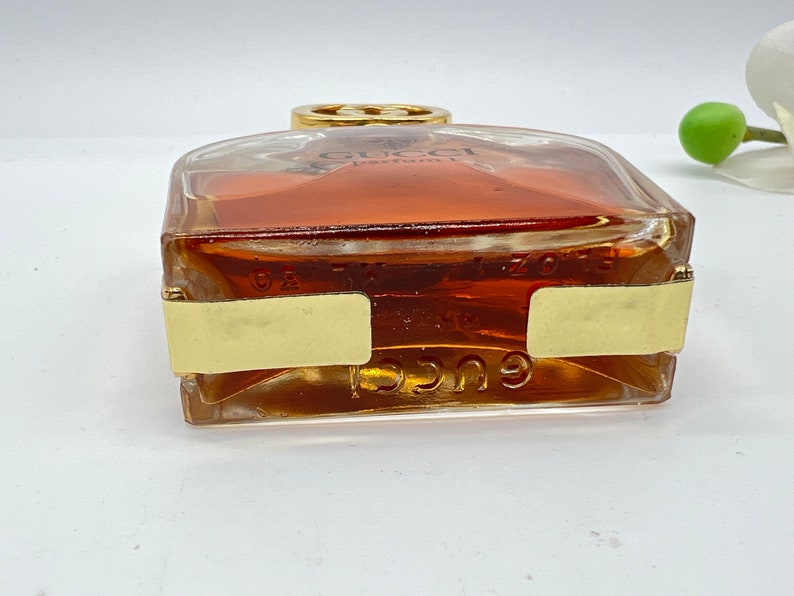 May include: A clear glass bottle of Gucci perfume with a gold cap and a gold label. The bottle is filled with a light brown liquid.