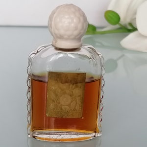 May include: A small, clear glass bottle with a white plastic stopper. The bottle contains a brown liquid and has a gold label with a floral design.