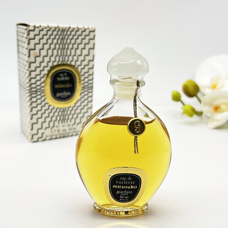 May include: A vintage bottle of Mitsouko Eau de Toilette by Guerlain. The bottle is clear glass with a gold cap and a gold label that reads "eau de toilette mitsouko guerlain paris 50 ml".