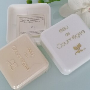 Puede incluir: Dos cajas cuadradas blancas con letras doradas. La caja superior dice "eau de Courr&egrave;ges" y la caja inferior dice "eau de Courr&egrave;ges".