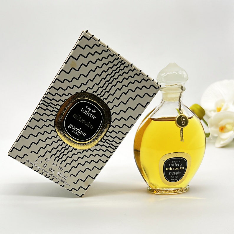 May include: A gold and white box with black text that reads "eau de toilette mitsouko guerlain PARIS 68, avenue des Champs-Elys&eacute;es 75008 Paris 1.7 fl. oz. 50 ml e N&deg; 381" and a clear glass bottle with a gold cap and label that reads "eau de toilette mitsouko guerlain 50 ml".
