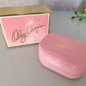 May include: A pink and gold bar soap in a box. The soap is labelled "Oleg Cassini II" and the box says "Savon Bath Soap".