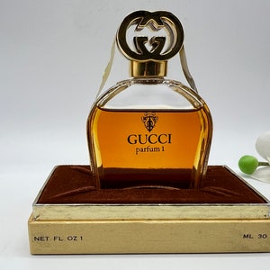 May include: A vintage Gucci perfume bottle in a brown box with gold trim. The bottle is clear glass with a gold cap and the words "GUCCI parfum 1" printed on the front. The box has the words "NET. FL. OZ 1" and "ML 30" printed on the bottom.