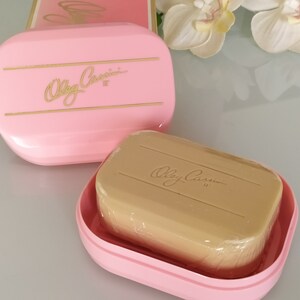 May include: A pink soap dish with a gold inscription that reads "Olga Cassini" and a beige bar of soap with the same inscription.