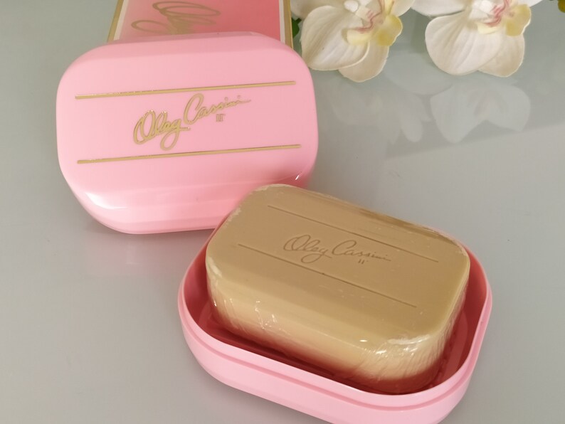 May include: A pink soap dish with a gold inscription that reads "Olga Cassini" and a beige bar of soap with the same inscription.