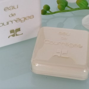 Puede incluir: Dos cajas blancas con el texto "eau de Courr&egrave;ges" y el logotipo "C" en dorado. Las cajas est&aacute;n sobre una superficie blanca.