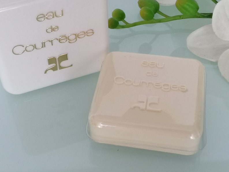 Puede incluir: Dos cajas blancas con el texto "eau de Courr&egrave;ges" y el logotipo "C" en dorado. Las cajas est&aacute;n sobre una superficie blanca.