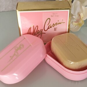 May include: A pink soap dish with a gold inscription of "Oleg Cassini II" on the lid. A bar of soap with the same inscription is inside the dish.
