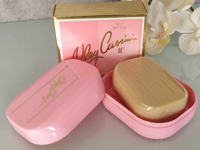 May include: A pink soap dish with a gold inscription of "Oleg Cassini II" on the lid. A bar of soap with the same inscription is inside the dish.