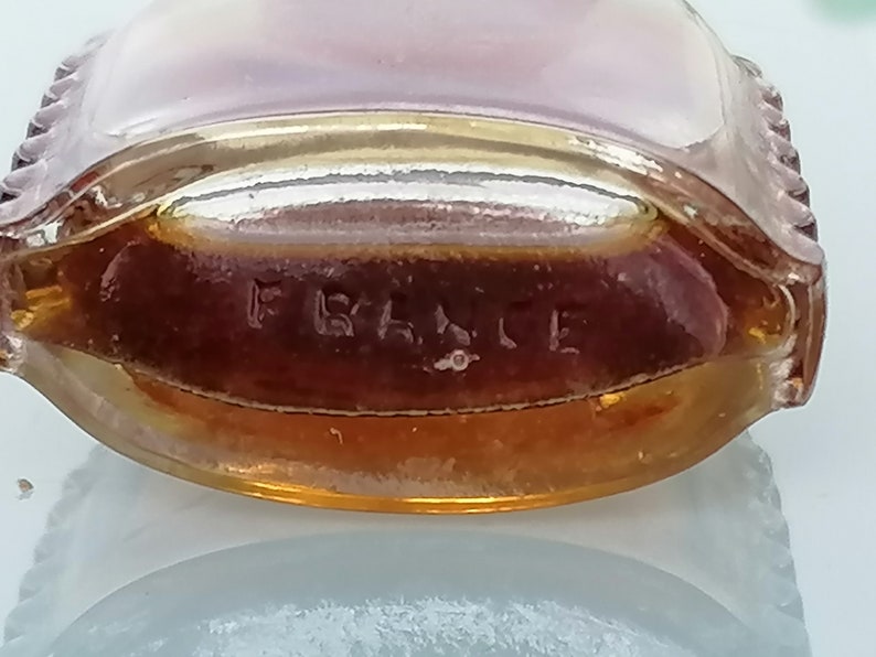 May include: A clear glass bottle with a gold rim and a brown liquid inside. The bottom of the bottle has the word "FRANCE" embossed on it.