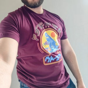 May include: A maroon t-shirt with a graphic of a blue dinosaur in front of a sunset. The dinosaur is standing on a beach with palm trees. The text "F*ck It" is written in Japanese characters below the dinosaur.