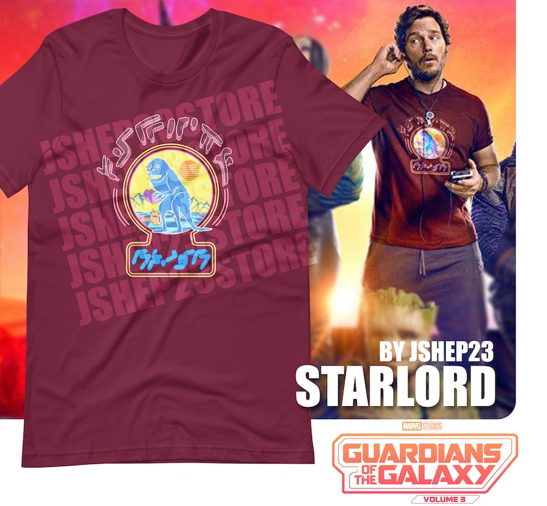 May include: A maroon t-shirt with a graphic of a blue dinosaur holding a blue orb. The graphic is surrounded by the text "JSHEP23STORE" in a white, blue, and yellow color scheme. The text "BY JSHEP23 STARLORD" is printed below the graphic. The text "GUARDIANS OF THE GALAXY VOLUME 3" is printed below the text "STARLORD".