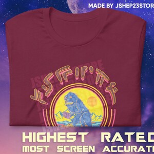May include: A maroon t-shirt with a retro-style graphic of a blue monster holding a purple rock. The graphic is surrounded by a yellow circle with a sunset in the background. The text "JShep23Store" is written in a stylized font around the graphic.