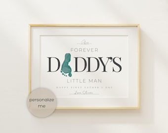 May include: A framed print with the text "FOREVER DADDY'S LITTLE MAN" in black. A teal footprint graphic is next to "DADDY'S". The print also includes "HAPPY FIRST FATHER'S DAY" and a signature. A circular sticker says "personalize me".