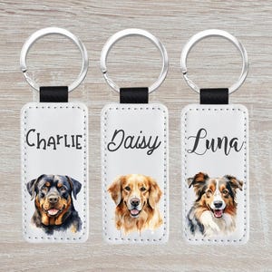 May include: Three white leather keychains with silver key rings. Each keychain features a different dog breed: a Rottweiler, a Golden Retriever, and an Australian Shepherd. The keychains are personalized with the names "Charlie", "Daisy", and "Luna" respectively.