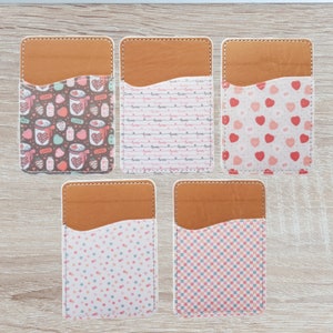 May include: Five brown leather card holders with different patterned inserts. The patterns include hearts, polka dots, checkered, and a pattern of jars with hearts and strawberries.