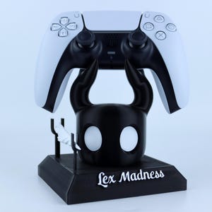 May include: A black and white 3D printed stand for a Playstation 5 controller. The stand features a stylized black and white character with the text "Lex Madness" printed on the base.