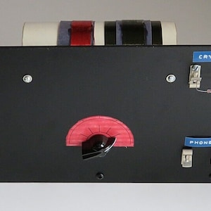 以下が含まれることがあります： 黒のパネルに赤と白のダイヤルと黒いノブが付いています。パネルには、"ANT"、"GND"、"CRYSTAL"、"PHONES"とラベル付けされた5つの銀色のクリップがあります。