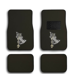 May include: Set of four black car floor mats with a rhinestone design of praying hands holding a cross. The front mats have a small black rectangle in the upper right corner.
