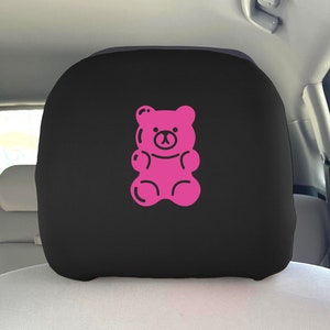 May include: Pink gummy bear shaped car headrest cover. The headrest cover is black with a pink gummy bear design.