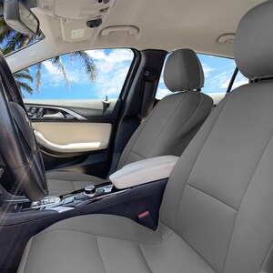 May include: Gray leather car seat covers installed in a car interior. The seats are gray with white stitching. The car has a black steering wheel and a white center console.