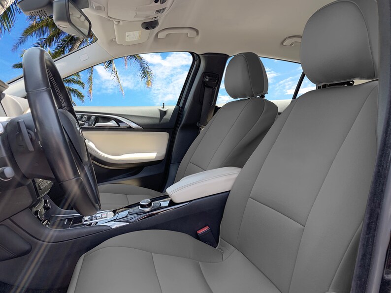 May include: Gray leather car seat covers installed in a car interior. The seats are gray with white stitching. The car has a black steering wheel and a white center console.
