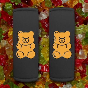 May include: Two black fabric can coolers with a yellow gummy bear design. The can coolers are surrounded by colorful gummy bears.